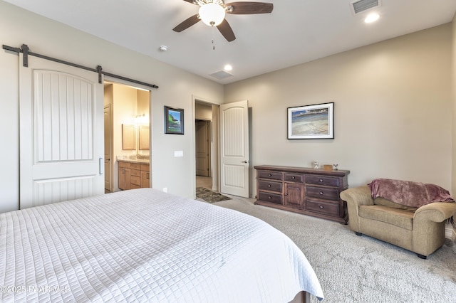 bedroom featuring visible vents, a ceiling fan, a barn door, ensuite bath, and carpet floors