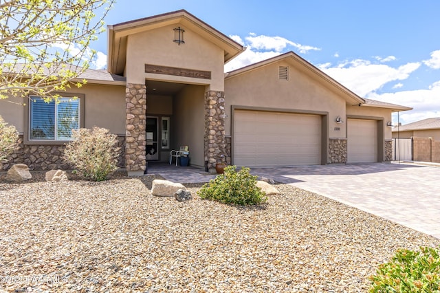 view of front of house featuring stone siding, driveway, fence, a garage, and stucco siding