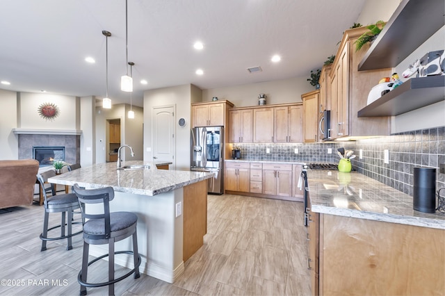 kitchen featuring a tile fireplace, appliances with stainless steel finishes, a sink, open shelves, and backsplash