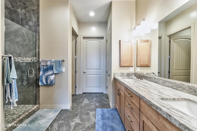 bathroom featuring double vanity, a sink, a stall shower, and baseboards