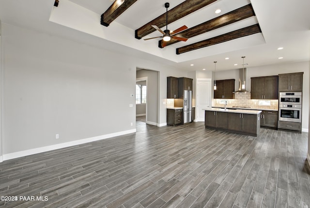 kitchen featuring wall chimney range hood, stainless steel appliances, tasteful backsplash, an island with sink, and decorative light fixtures