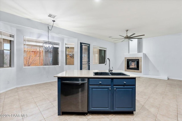 kitchen with blue cabinetry, light countertops, stainless steel dishwasher, a sink, and a tile fireplace