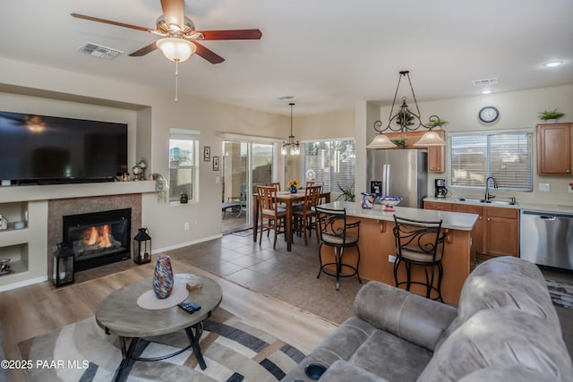 living room with ceiling fan with notable chandelier, sink, a tile fireplace, and light hardwood / wood-style flooring