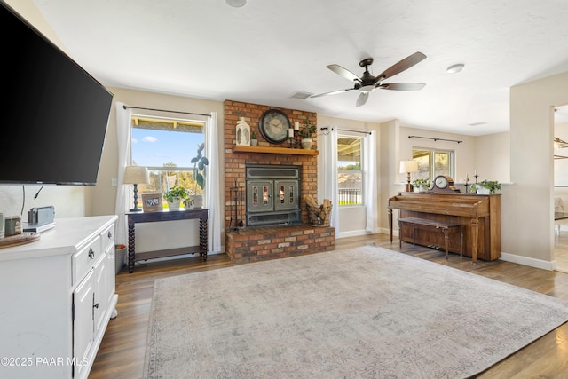 living room with a healthy amount of sunlight, a wood stove, dark wood-type flooring, and ceiling fan