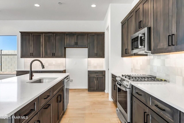 kitchen with appliances with stainless steel finishes, tasteful backsplash, sink, dark brown cabinetry, and light hardwood / wood-style flooring