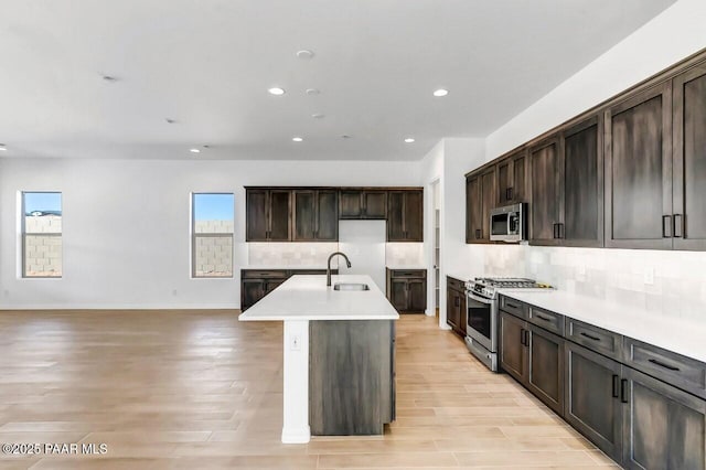 kitchen with sink, appliances with stainless steel finishes, tasteful backsplash, an island with sink, and light wood-type flooring