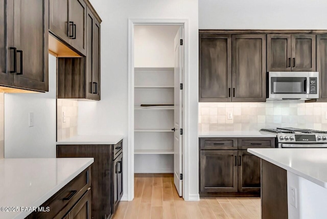 kitchen with tasteful backsplash, appliances with stainless steel finishes, light hardwood / wood-style floors, and dark brown cabinets