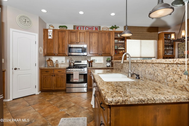 kitchen featuring light stone countertops, sink, stainless steel appliances, pendant lighting, and decorative backsplash