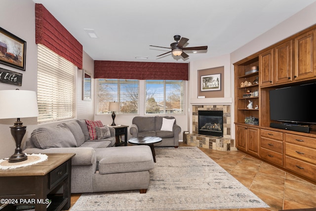 tiled living room featuring built in shelves, a healthy amount of sunlight, a stone fireplace, and ceiling fan