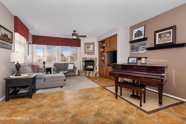 tiled living room featuring built in shelves, ceiling fan, and a stone fireplace