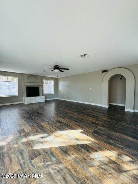 unfurnished living room featuring arched walkways, a fireplace with raised hearth, visible vents, baseboards, and dark wood finished floors