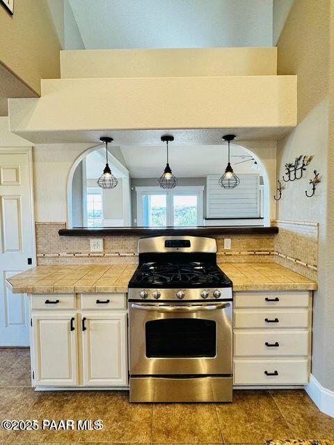 kitchen featuring tasteful backsplash, white cabinets, stainless steel range with gas stovetop, and decorative light fixtures