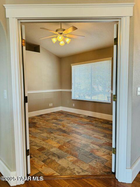 spare room featuring dark wood-style flooring, a ceiling fan, and baseboards