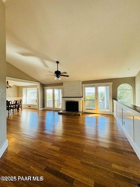 unfurnished living room featuring lofted ceiling, a fireplace with raised hearth, wood finished floors, baseboards, and ceiling fan with notable chandelier