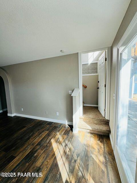 interior space featuring baseboards, arched walkways, dark wood finished floors, and a textured ceiling