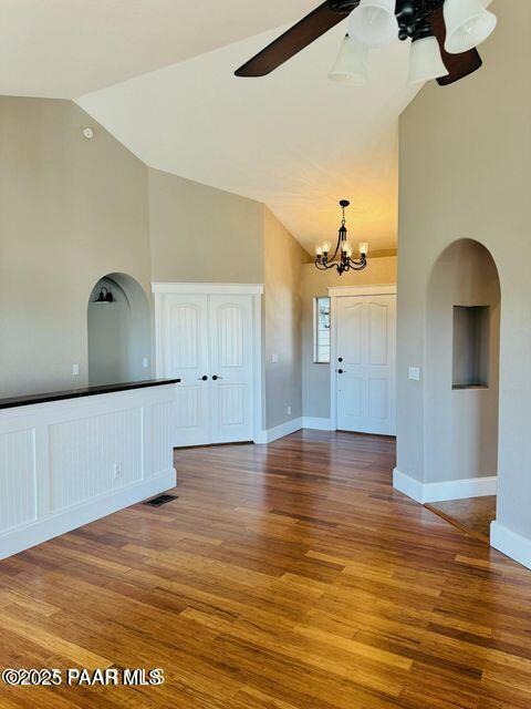 interior space with arched walkways, high vaulted ceiling, ceiling fan with notable chandelier, wood finished floors, and baseboards