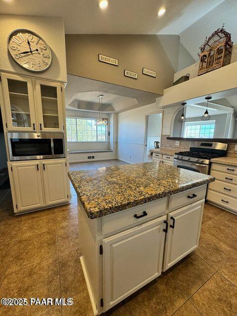 kitchen featuring stainless steel appliances, white cabinetry, a kitchen island, and glass insert cabinets