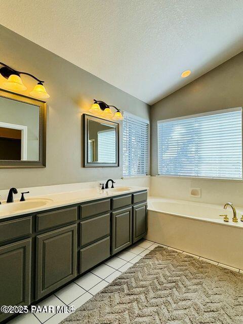 bathroom with double vanity, tile patterned floors, vaulted ceiling, a sink, and a bath