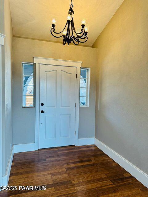 foyer entrance with vaulted ceiling, dark wood-type flooring, baseboards, and an inviting chandelier