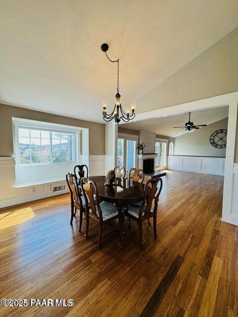 dining space featuring a notable chandelier, dark wood-type flooring, wainscoting, vaulted ceiling, and a textured ceiling