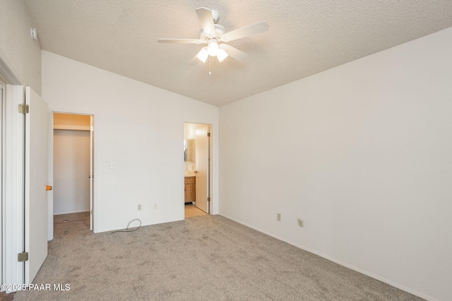 unfurnished bedroom with a spacious closet, light carpet, a textured ceiling, and vaulted ceiling