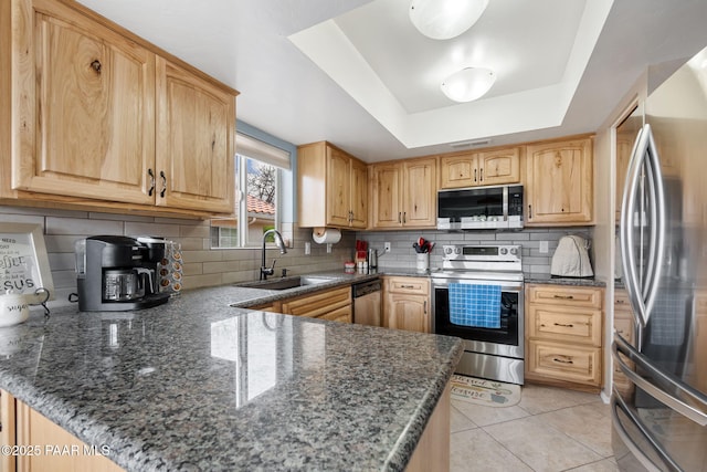 kitchen featuring appliances with stainless steel finishes, a sink, a raised ceiling, backsplash, and a peninsula