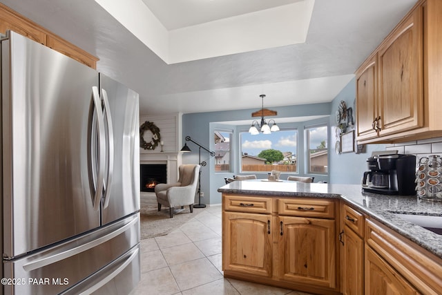 kitchen featuring freestanding refrigerator, a peninsula, light tile patterned flooring, pendant lighting, and a large fireplace