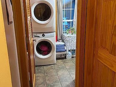 laundry room featuring stacked washing maching and dryer and tile floors