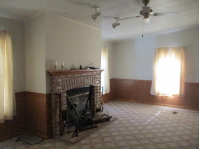 living room featuring ceiling fan, rail lighting, wood walls, a fireplace, and ornamental molding