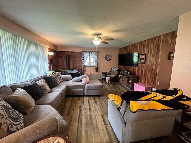 living room with a textured ceiling, ceiling fan, wooden walls, hardwood / wood-style floors, and a wood stove