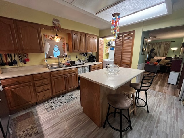 kitchen with a center island, hanging light fixtures, sink, light hardwood / wood-style floors, and a breakfast bar area