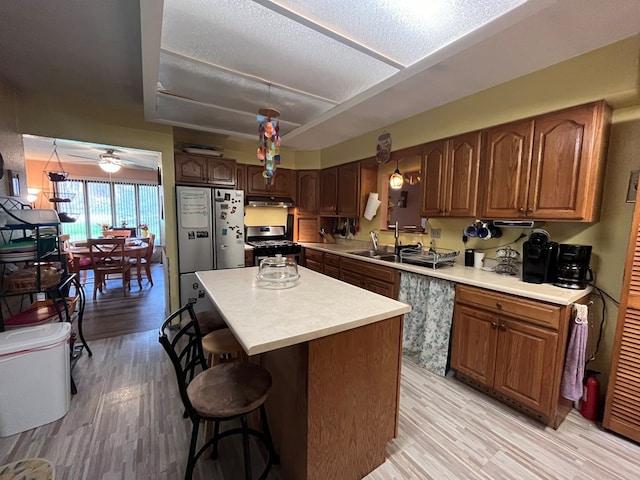 kitchen with ceiling fan, appliances with stainless steel finishes, a textured ceiling, a kitchen island, and light wood-type flooring