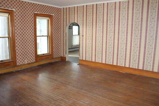 empty room featuring dark wood-type flooring, baseboard heating, and ornamental molding