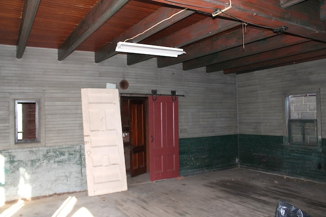 empty room with beamed ceiling, a barn door, wood-type flooring, and wooden walls