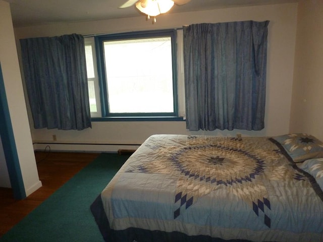 bedroom featuring ceiling fan, dark hardwood / wood-style floors, multiple windows, and a baseboard heating unit