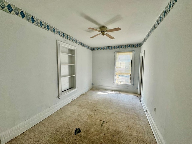 empty room featuring light carpet, built in features, and ceiling fan