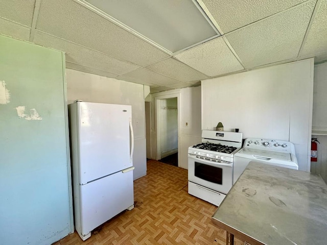 kitchen with a drop ceiling, light parquet flooring, white appliances, and washer / dryer