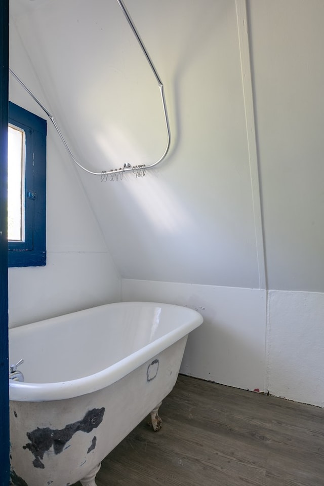 bathroom with lofted ceiling, hardwood / wood-style floors, and a tub to relax in