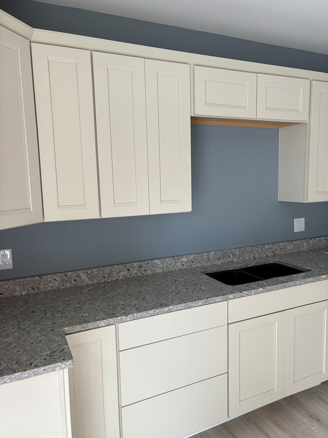 kitchen featuring sink, stone counters, white cabinets, and light wood-type flooring