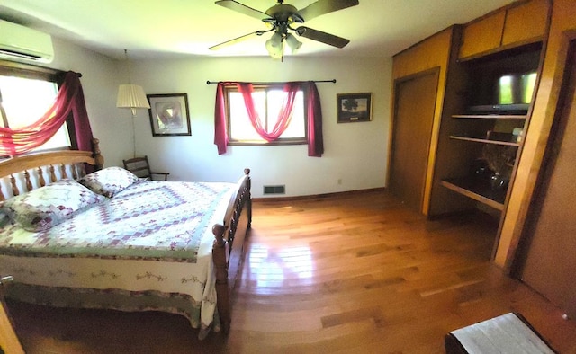 bedroom featuring a wall mounted air conditioner, hardwood / wood-style floors, and ceiling fan