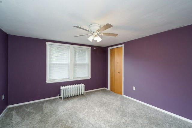 empty room featuring ceiling fan, radiator heating unit, and carpet floors