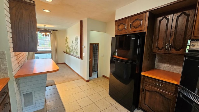 kitchen featuring dark brown cabinets, light tile patterned flooring, decorative light fixtures, and black refrigerator