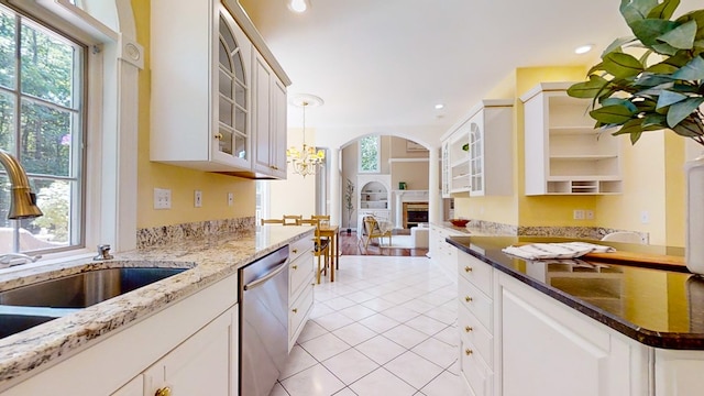 kitchen with sink, decorative light fixtures, light tile patterned floors, stainless steel dishwasher, and dark stone counters