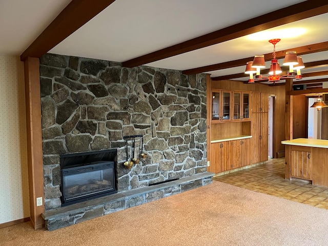 unfurnished living room with an inviting chandelier, a stone fireplace, light colored carpet, and beam ceiling