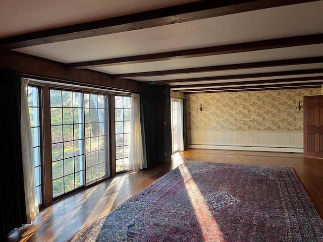 empty room with a baseboard radiator, plenty of natural light, beam ceiling, and hardwood / wood-style floors