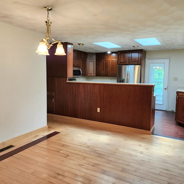 kitchen with kitchen peninsula, a skylight, stainless steel appliances, light hardwood / wood-style floors, and hanging light fixtures