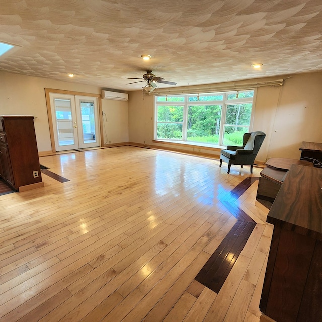 living room with a wall mounted air conditioner, ceiling fan, a textured ceiling, and light hardwood / wood-style flooring