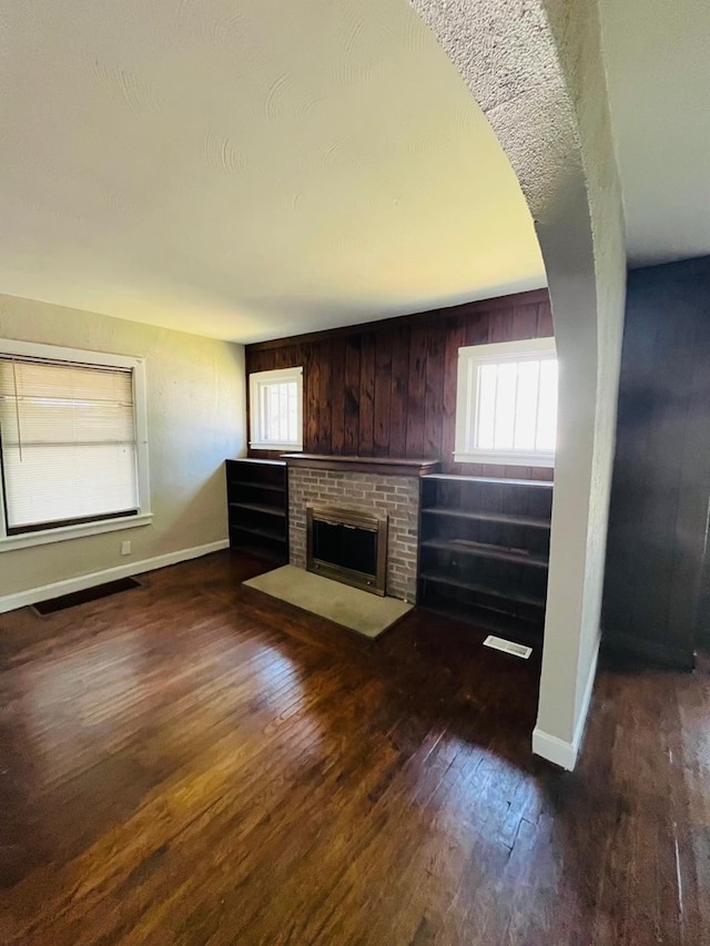 unfurnished living room featuring a brick fireplace, wood walls, and dark hardwood / wood-style floors