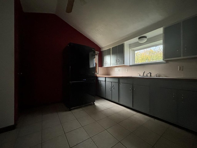 kitchen featuring light tile patterned floors, decorative backsplash, vaulted ceiling, and black refrigerator