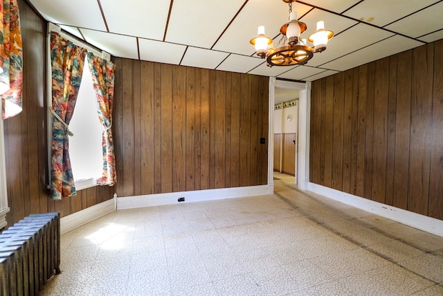 empty room featuring radiator, wooden walls, and a notable chandelier